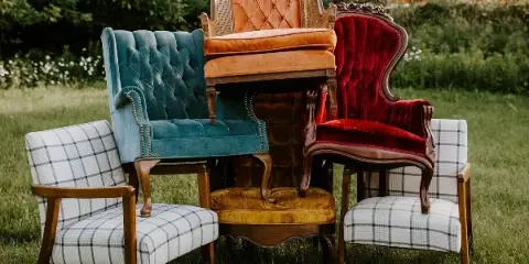 A group of vintage upholstered armchairs and a velvet chair arranged on a grassy lawn.
