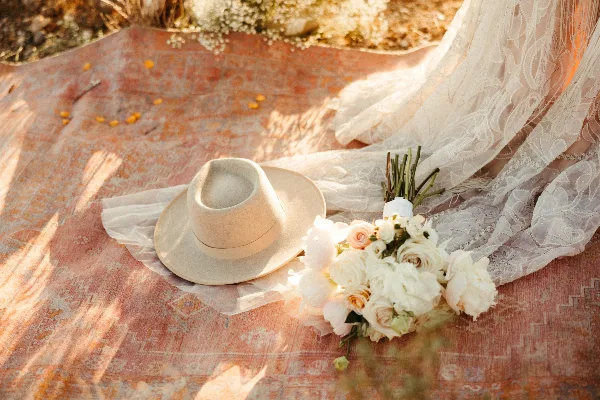 A wedding bouquet and hat resting on a patterned rug next to a lace veil.