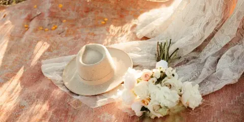 A wedding bouquet and hat resting on a patterned rug next to a lace veil.