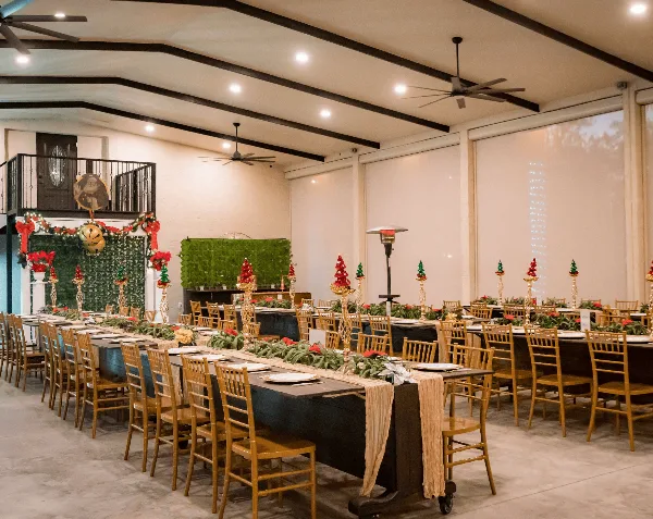 Interior view of a wedding venue event space with long tables, wooden chairs, and holiday decorations.