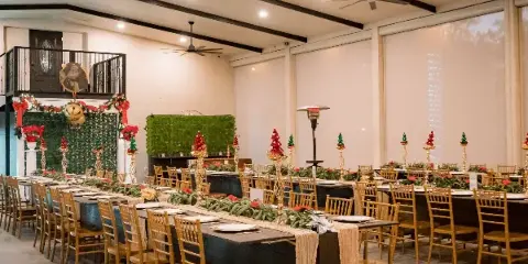 Interior view of a wedding venue event space with long tables, wooden chairs, and holiday decorations.