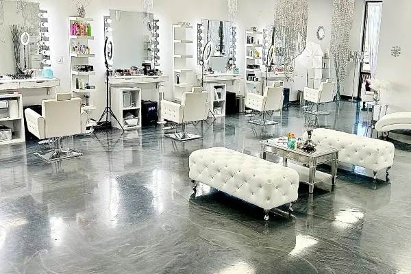 Interior view of a makeup studio featuring white chairs, vanity mirrors with lights, and product shelves.