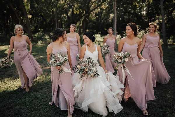 A bride and bridesmaids in a wooded area holding large, custom wedding floral bouquets.