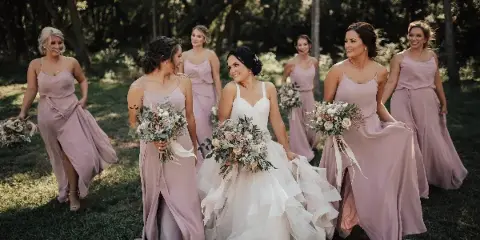 A bride and bridesmaids in a wooded area holding large, custom wedding floral bouquets.