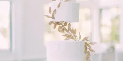 A five-tier white wedding cake with textured frosting and gold leaf decorations on a table.