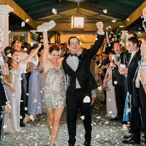 A bride and groom celebrating at a wedding reception with guests and flower petals in the air.