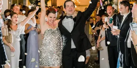 A bride and groom celebrating at a wedding reception with guests and flower petals in the air.