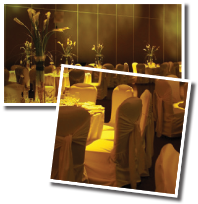 A banquet hall set up for a formal event with white tablecloths, draped chairs, and floral centerpieces.