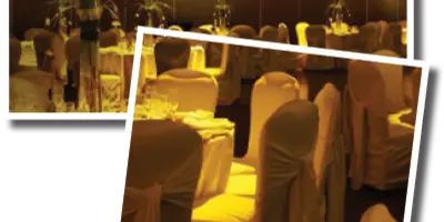 A banquet hall set up for a formal event with white tablecloths, draped chairs, and floral centerpieces.