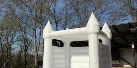 A white castle-themed inflatable bounce house set up outdoors on a lawn.
