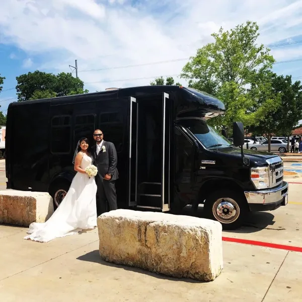 A bride and groom standing in front of a black shuttle bus