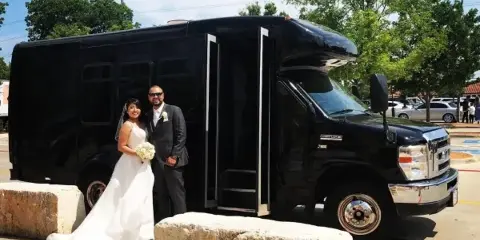 A bride and groom standing in front of a black shuttle bus