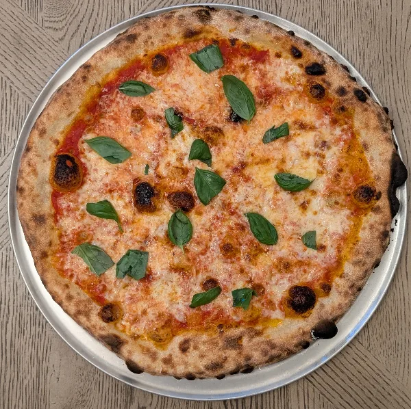A whole Margherita pizza with basil leaves and melted cheese on a metal tray.