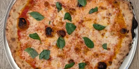 A whole Margherita pizza with basil leaves and melted cheese on a metal tray.