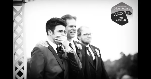 A black and white photograph of a groom covering his mouth with his hand, standing with his groomsmen during a wedding ceremony.