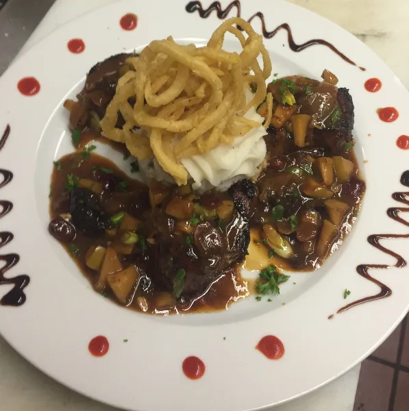 A plated meal with meat, mashed potatoes, and fried garnish on a white plate with sauce accents.