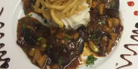 A plated meal with meat, mashed potatoes, and fried garnish on a white plate with sauce accents.