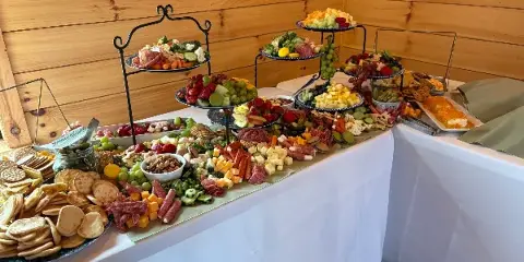 A catering buffet table featuring a charcuterie board, fruit platters, and assorted appetizers.