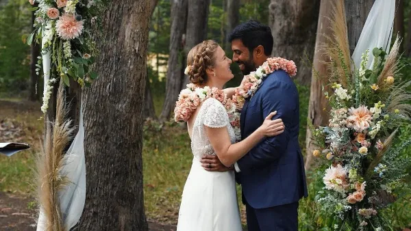 A bride and groom embracing during a wedding ceremony in a forest setting.