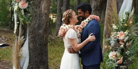 A bride and groom embracing during a wedding ceremony in a forest setting.