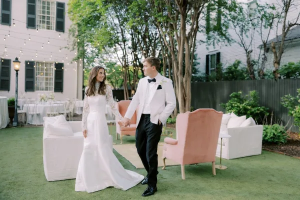 A bride and groom standing in an outdoor lounge area furnished with a peach velvet armchair and white sofa.