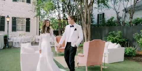 A bride and groom standing in an outdoor lounge area furnished with a peach velvet armchair and white sofa.