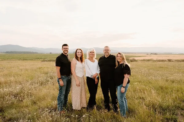 A group of five people standing in a grassy field with mountains in the background.