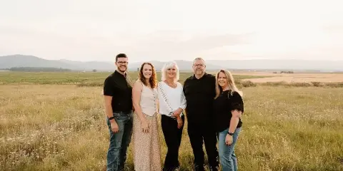 A group of five people standing in a grassy field with mountains in the background.