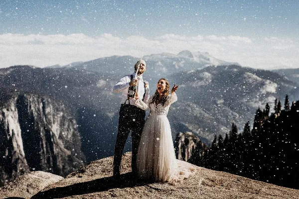 A bride and groom celebrating with a champagne spray on a rocky mountain overlook.