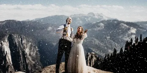A bride and groom celebrating with a champagne spray on a rocky mountain overlook.