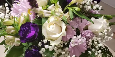 A floral arrangement featuring white roses, purple lisianthus, pink daisies, and baby's breath in a glass vase.