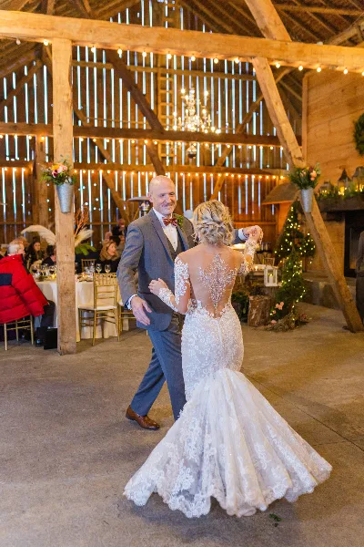 A bride and groom dancing inside a rustic wooden barn event venue with string lights and a chandelier.
