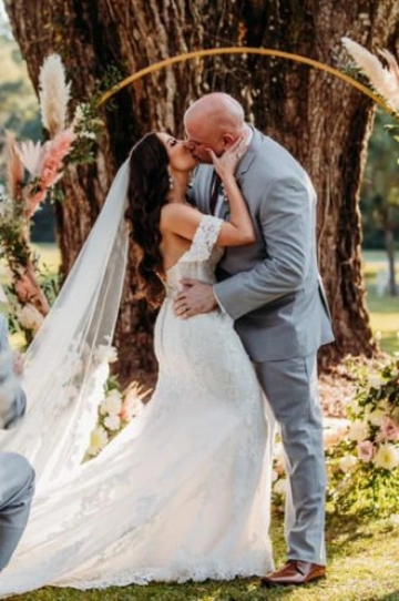 A bride and groom sharing a kiss during an outdoor wedding ceremony under a floral arch.