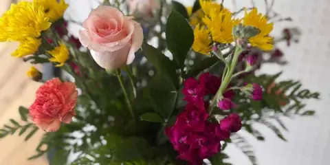 A close-up of a fresh flower bouquet containing a pink rose, yellow chrysanthemums, and purple stock flowers arranged in a vase.