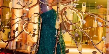 A model with dramatic makeup and an elaborate headpiece standing in front of a large, artistic metal sculpture with champagne flutes.
