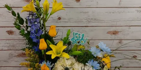 Mixed floral arrangement with yellow lilies, blue flowers, and white hydrangea in a wooden box