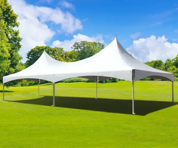 A white high-top frame tent set up on a green lawn under a blue sky.