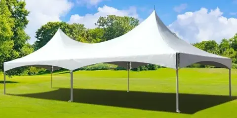A white high-top frame tent set up on a green lawn under a blue sky.