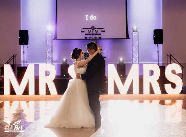 A bride and groom dancing at a wedding reception with professional stage lighting and sound equipment in the background.
