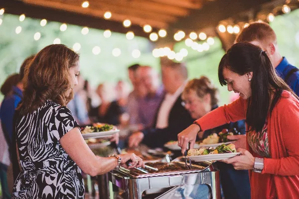 Guests serving themselves food from a buffet line at an outdoor event.