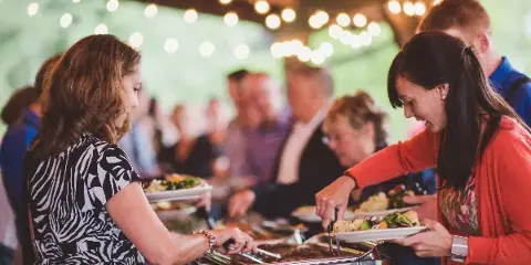 Guests serving themselves food from a buffet line at an outdoor event.