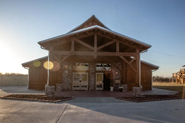 Exterior view of a timber frame lodge-style wedding venue with stone accents and a metal roof, situated on open farmland.