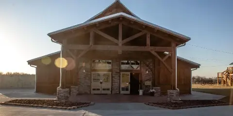 Exterior view of a timber frame lodge-style wedding venue with stone accents and a metal roof, situated on open farmland.