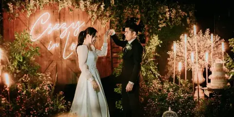 A bride and groom dancing at a wedding reception with floral decorations and a neon sign in the background.