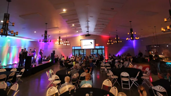 Interior view of a large event hall with a band on stage and guests seated at round tables.