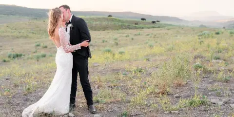 A bride and groom sharing a kiss in a grassy field with rolling hills in the background.