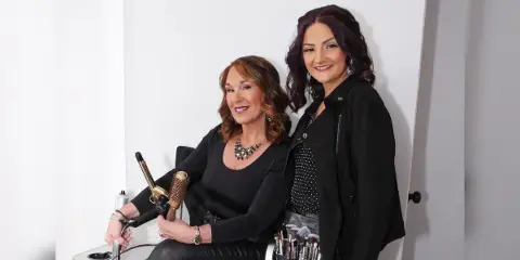 Two women posing with professional hair styling tools and makeup brushes.