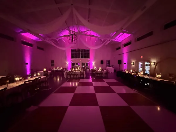 A wedding reception hall featuring a checkered dance floor and vibrant magenta uplighting.