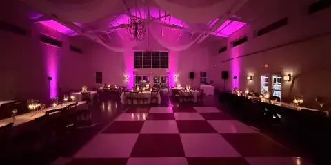 A wedding reception hall featuring a checkered dance floor and vibrant magenta uplighting.