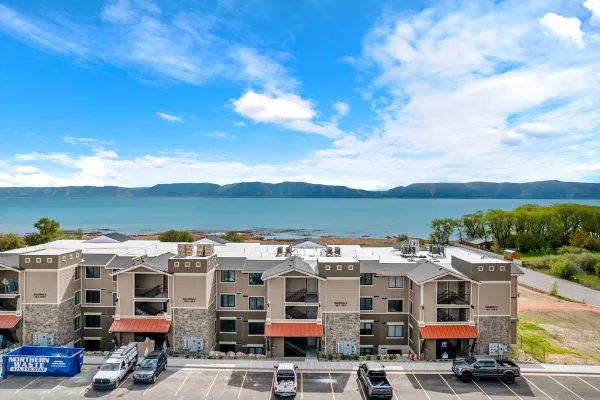 Aerial view of the Water's Edge Resort condominium buildings situated directly on the shore of Bear Lake with mountains in the background.
